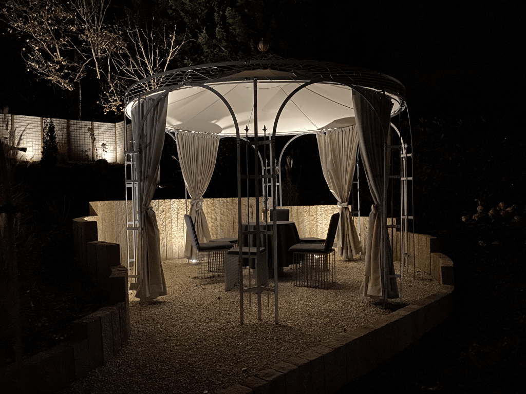 Pavillon Florenz pulverbeschichtet anthrazit mit Messingkugel und Sonnensegel beleuchtet bei Nacht in einem Garten