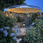 Pavillon Florenz pulverbeschichtet anthrazit mit Messingkugel und Sonnensegel mit Lichterkette in einem Garten