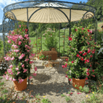 Pavillon Florenz pulverbeschichtet anthrazit mit Messingkugel und Sonnensegel in Ecru in einem Garten