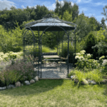 Pavillon Milano pulverbeschichtet anthrazit mit Messingkugel und Sonnensegel in Dunkelgrün in einem Garten