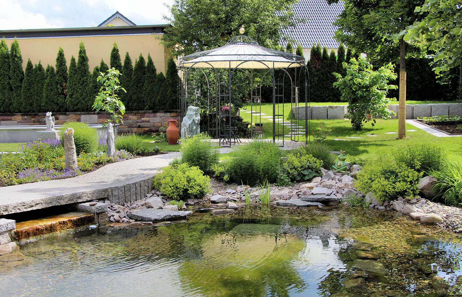 Pavillon Florenz mit Messingkugel und Sonnensegel in pulverbeschichteter Ausführung in einem schönen Garten mit Teich und Pool