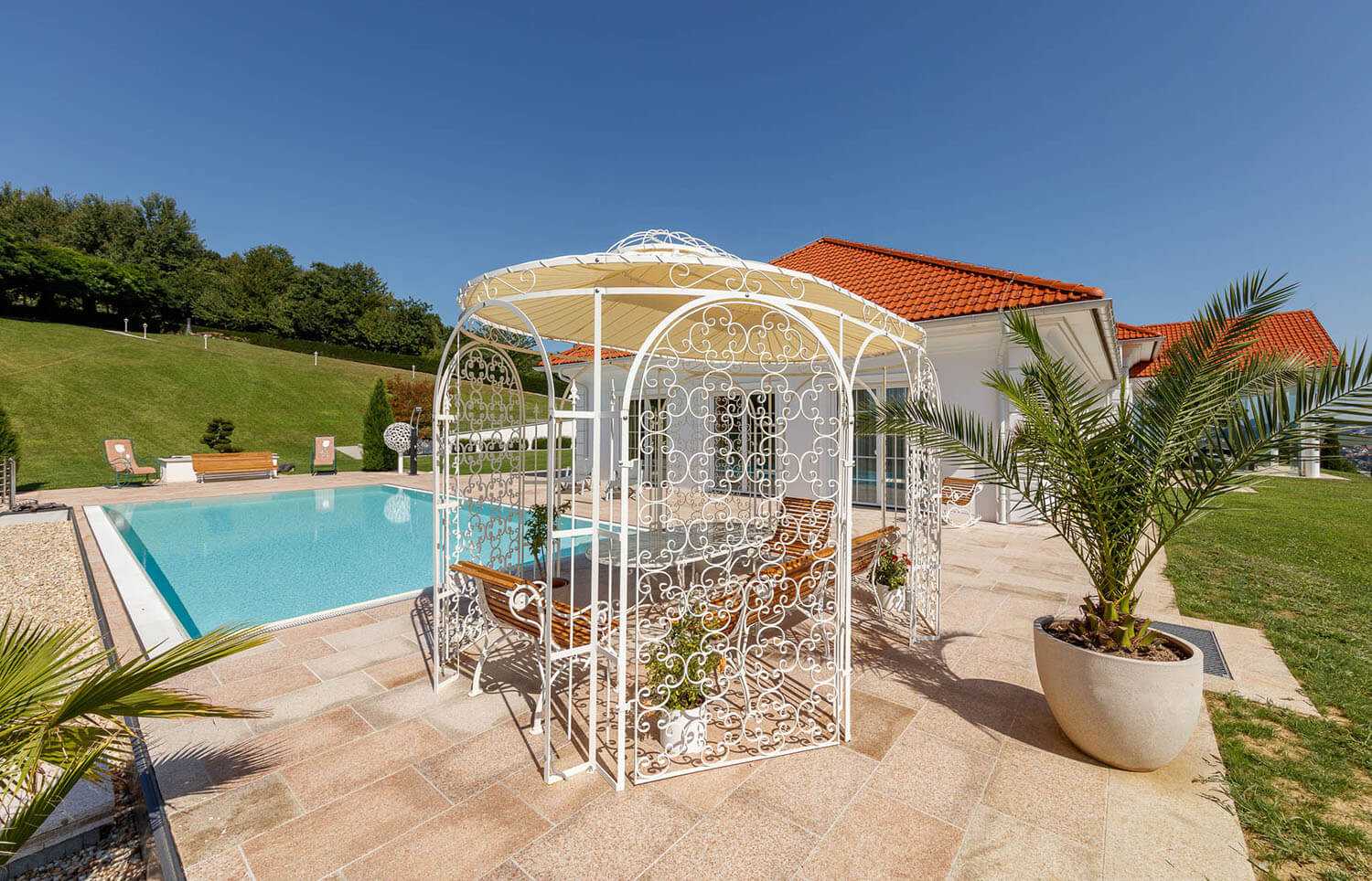 Pavillon Verona in pulverbeschichteter Sonderfarbe mit Sonnensegel und Rankgitter vor modernen Pool