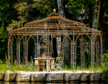 Pavillon Toskana in unbeschichtet mit Holzstuehlen hinter einem Teich