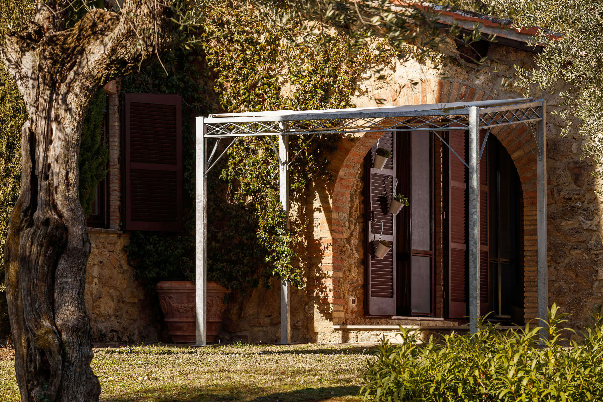 Pergola Ischia in feuerverzinkter Ausführung an einer terrasse angelehnt mit Sonnensegel