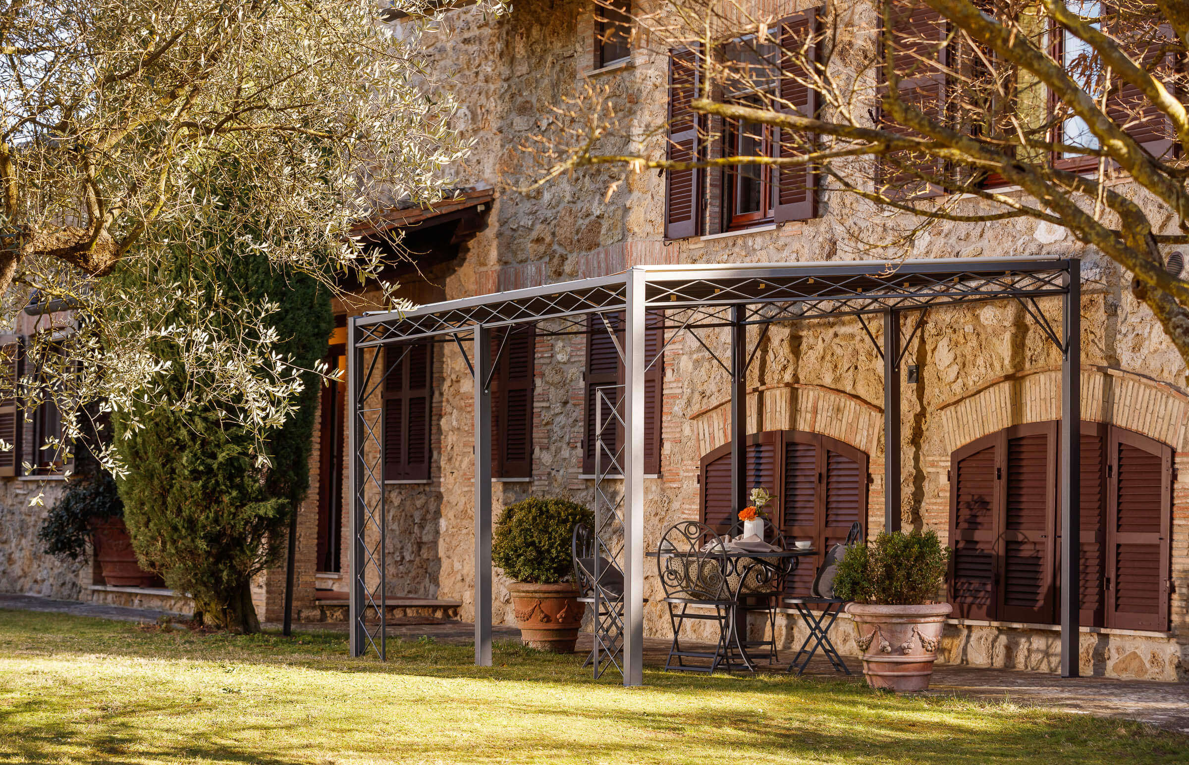 Pergola Sicilia in pulverbeschichteter Ausführung mit Sonnensegel an altmodernen Sandsteinhaus in der Toskana