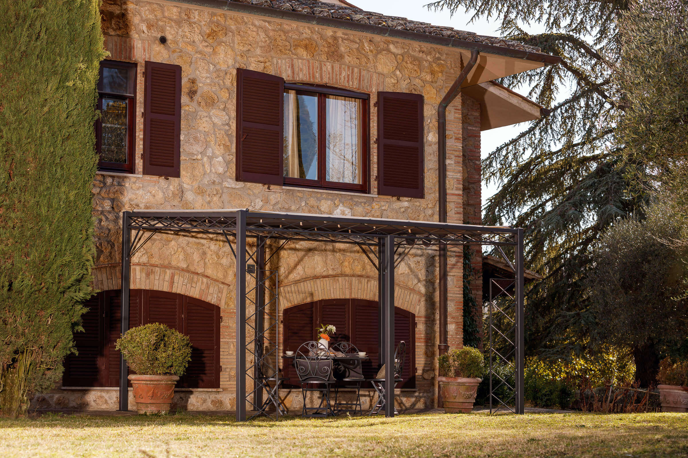 Pergola Sicilia in pulverbeschichteter Ausführung mit Sonnensegel und Rankgitter Vite an altmodernen Sandsteinhaus in der Toskana