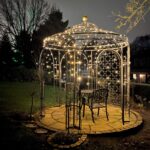 Pavillon Milano pulverbeschichtet Anthrazit mit Messingkugel und Rankgitter Rosa beleuchtet in einem Garten