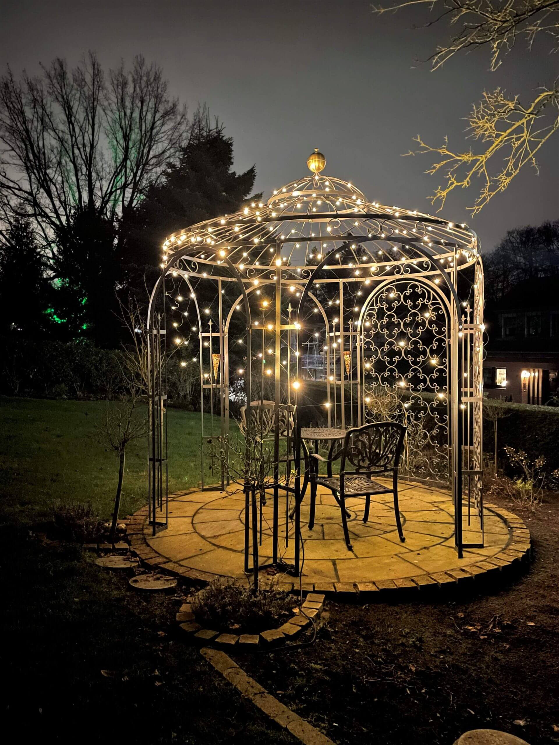 Pavillon Milano pulverbeschichtet Anthrazit mit Messingkugel und Rankgitter Rosa beleuchtet in einem Garten